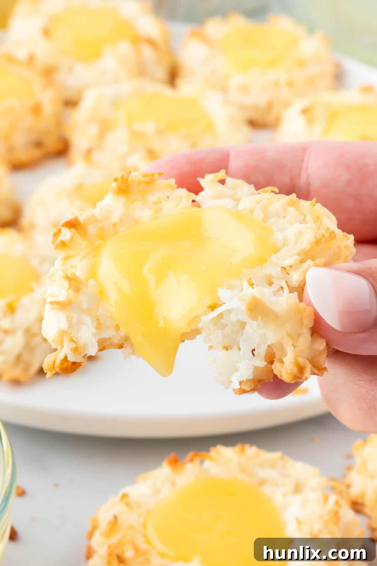 A hand holding a lemon curd coconut macaroon, with a bite taken out, revealing the soft coconut interior and bright lemon curd filling.