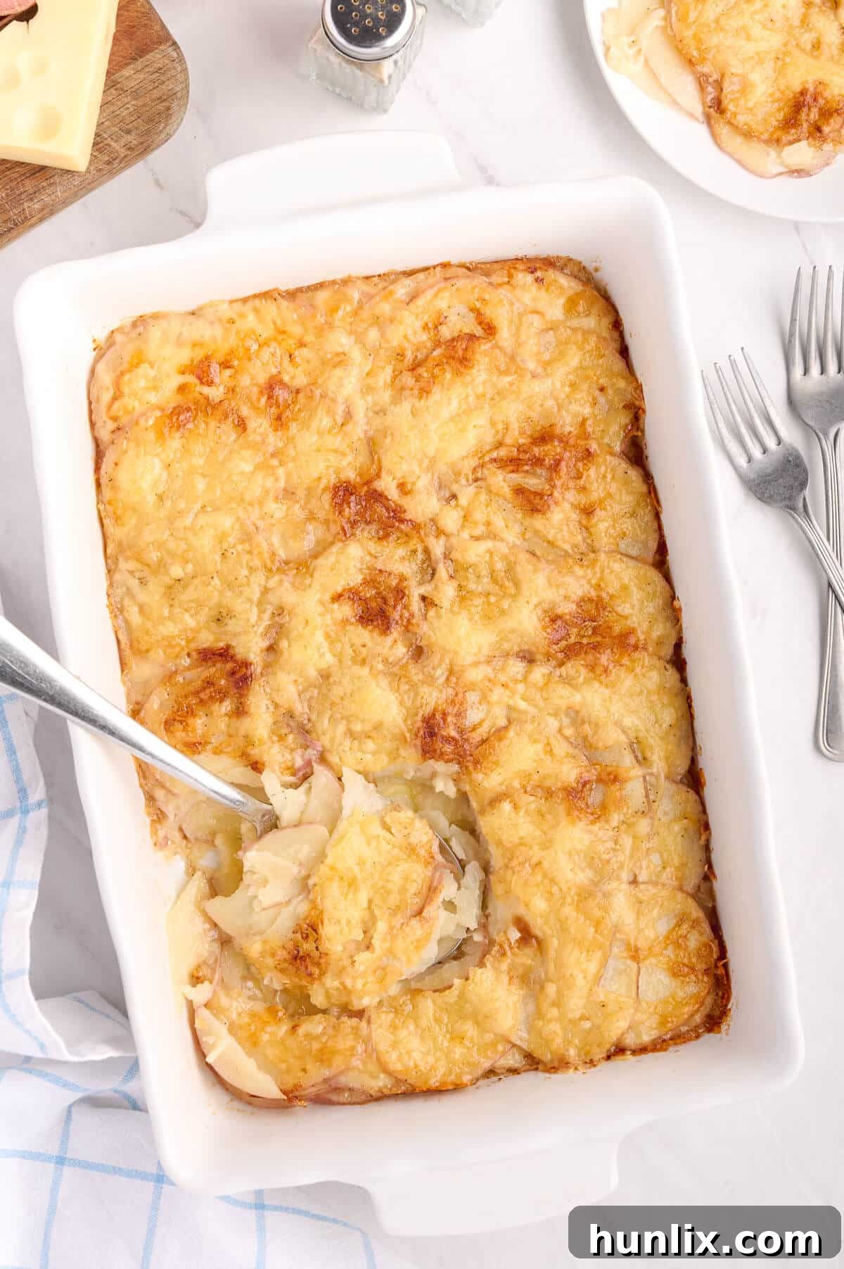 A baking pan of Swiss Potatoes with a serving spoon.