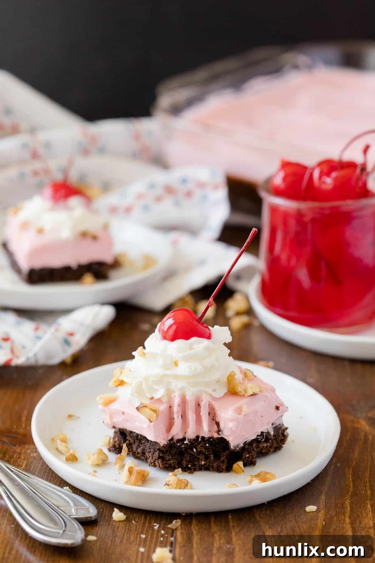 A delectable slice of Banana Split Brownie, with a bite taken out, showcasing the moist brownie base, creamy strawberry frosting, and a hint of a cherry.