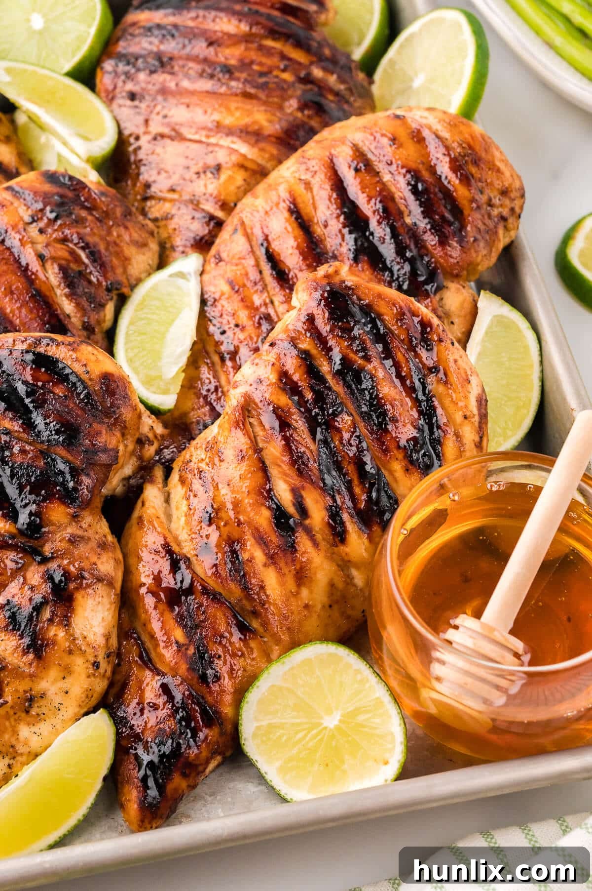 Ginger Lime Chicken on a platter, garnished with fresh limes and a small dish of honey.