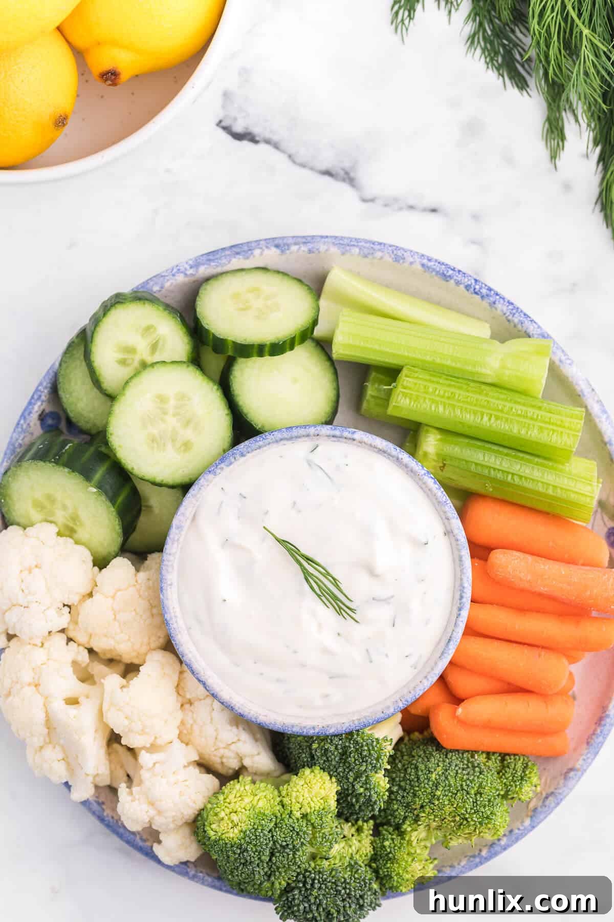 Fresh Lemon Dill Dip on a wooden board with an assortment of crisp vegetables, highlighting its creamy texture and vibrant green dill flecks.