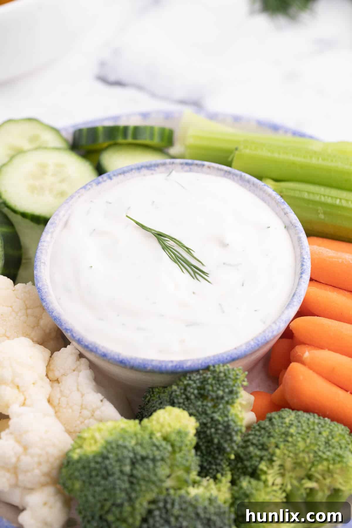 A hand dipping a fresh carrot stick into a creamy Lemon Dill Dip in a white bowl, ready for a healthy snack.