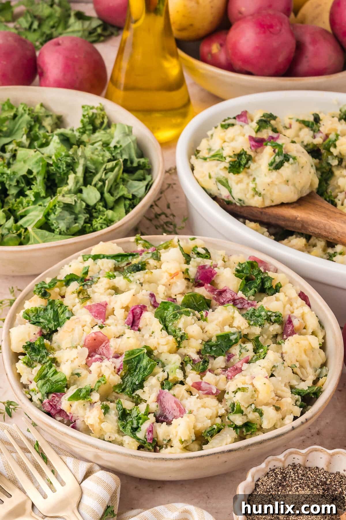 A beautifully presented bowl of olive oil mashed potatoes with kale and herbs, ready to be served, on a light-colored surface.