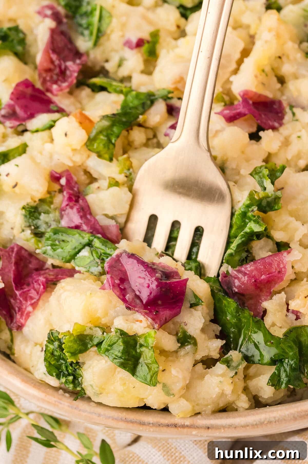 A plated serving of olive oil mashed potatoes with kale and herbs, garnished with a sprig of fresh thyme, alongside a fork.