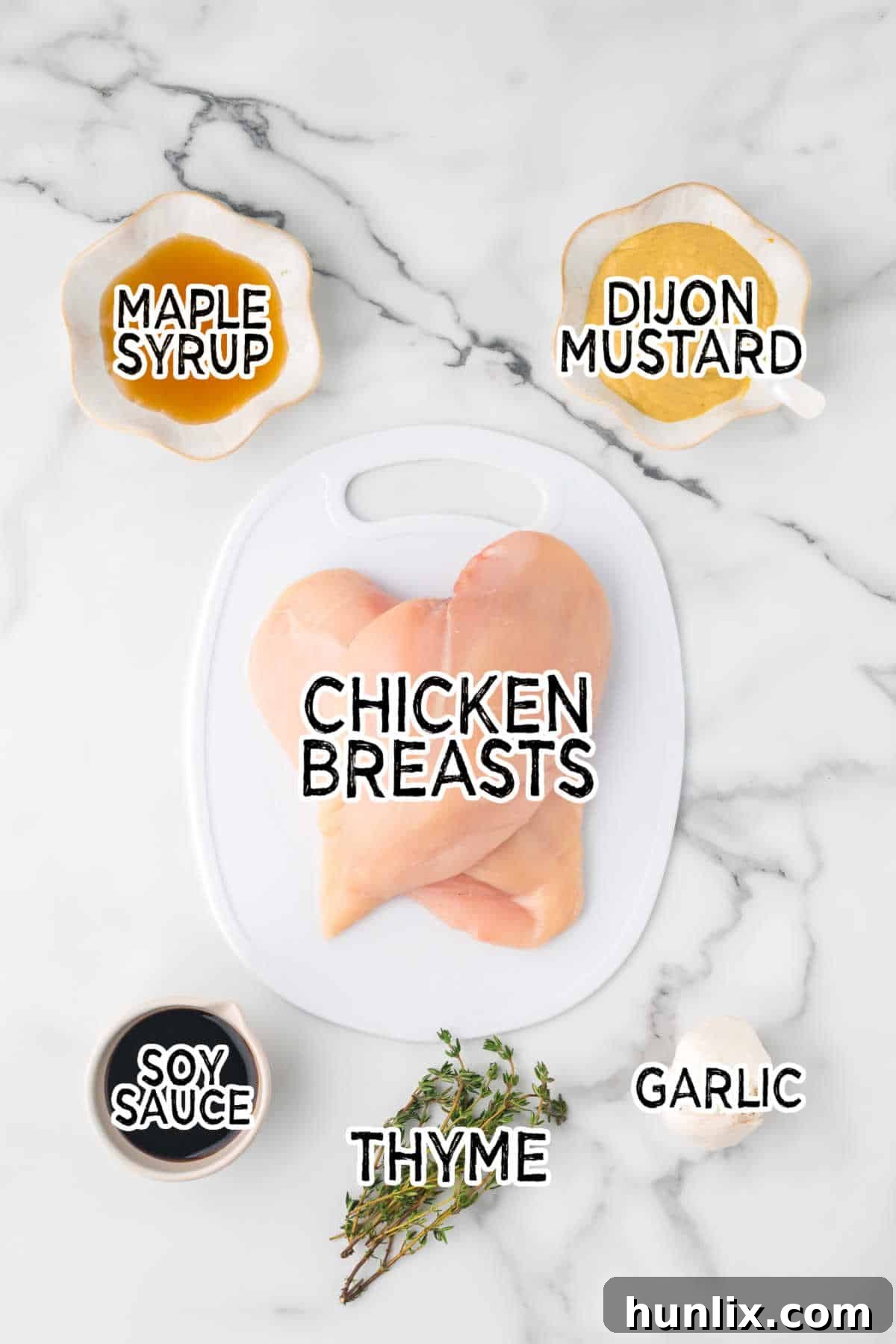 Ingredients for maple dijon grilled chicken laid out on a white countertop: chicken breasts, maple syrup, Dijon mustard, soy sauce, fresh thyme, and garlic.