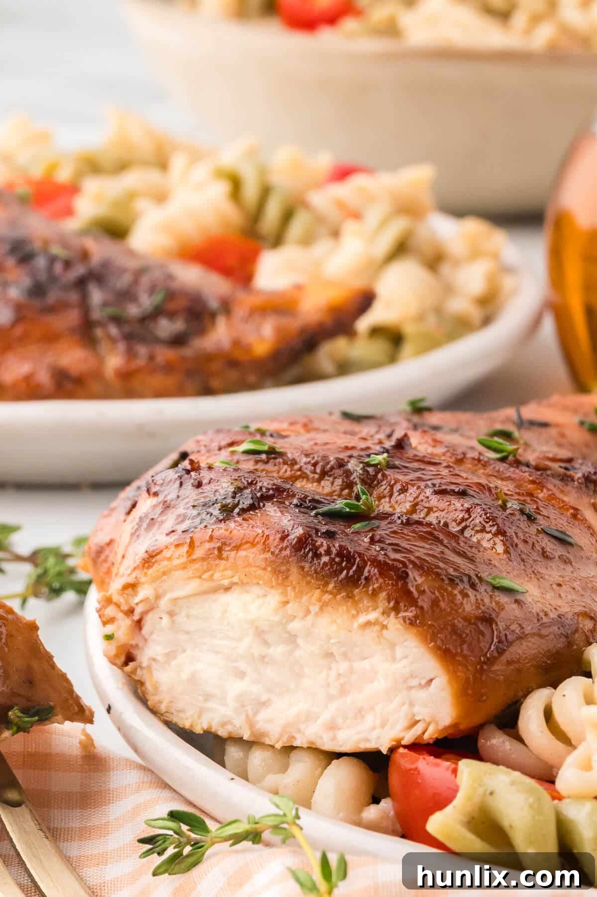 Sliced maple dijon grilled chicken breast beautifully arranged on top of a pasta salad on a plate.