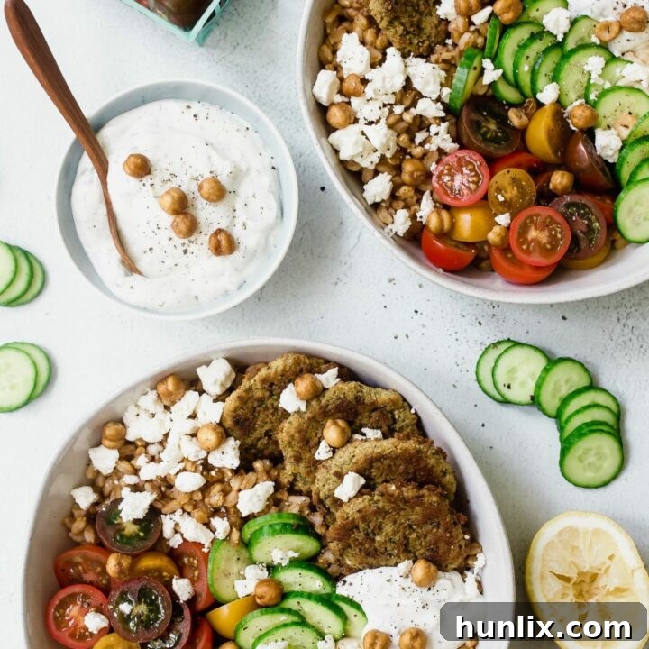 Baked Falafel Bowls with crisp cucumbers, juicy tomatoes, crumbled feta, creamy hummus, and cool tzatziki sauce piled high on a bed of nutty farro.