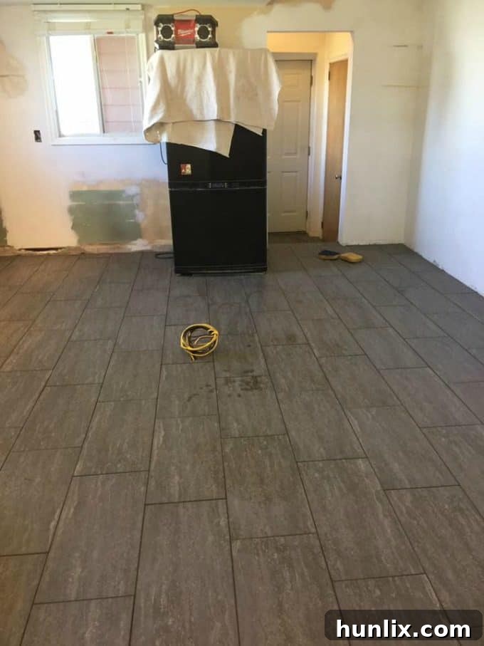 Kitchen renovation progress: Walls primed and new floor tiles being installed, with the old fridge remaining