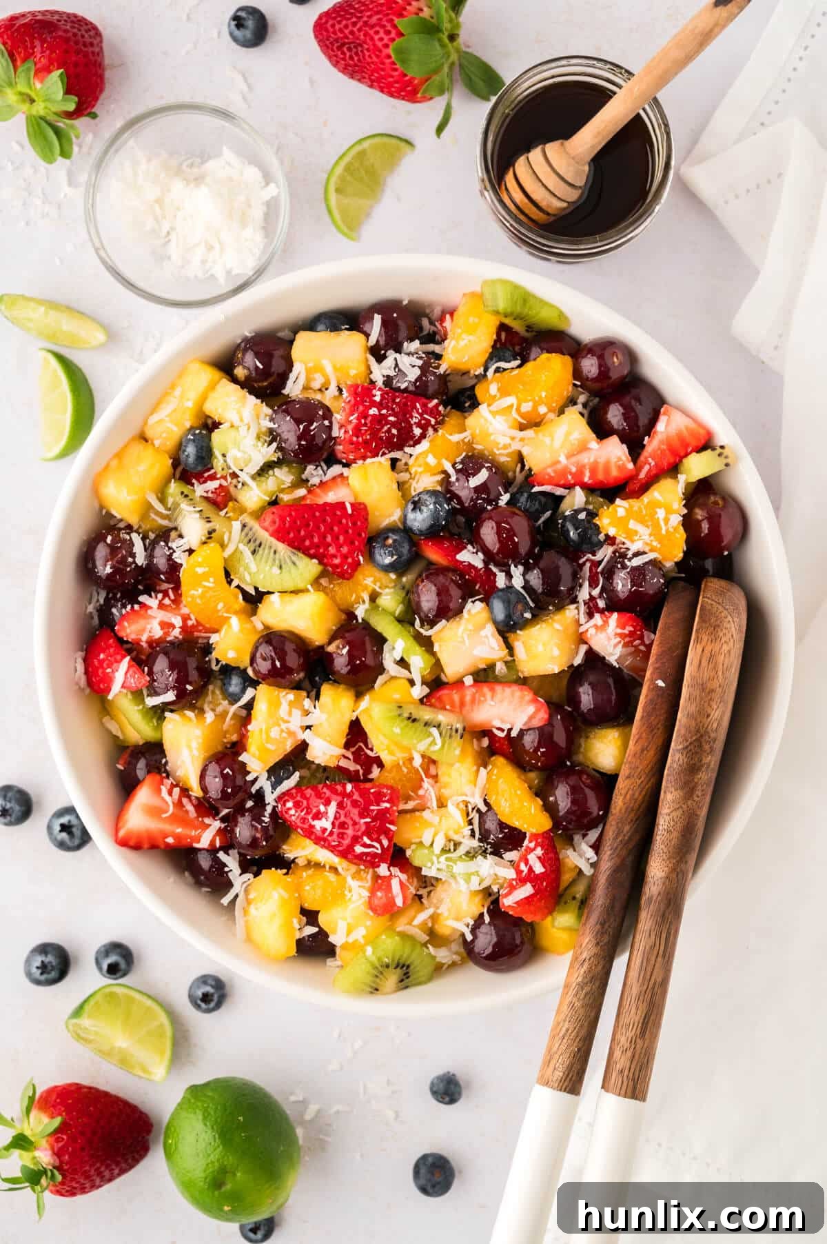 A vibrant bowl of rainbow fruit salad, showcasing a spectrum of fresh fruits, served with wooden tongs, ready to be enjoyed.