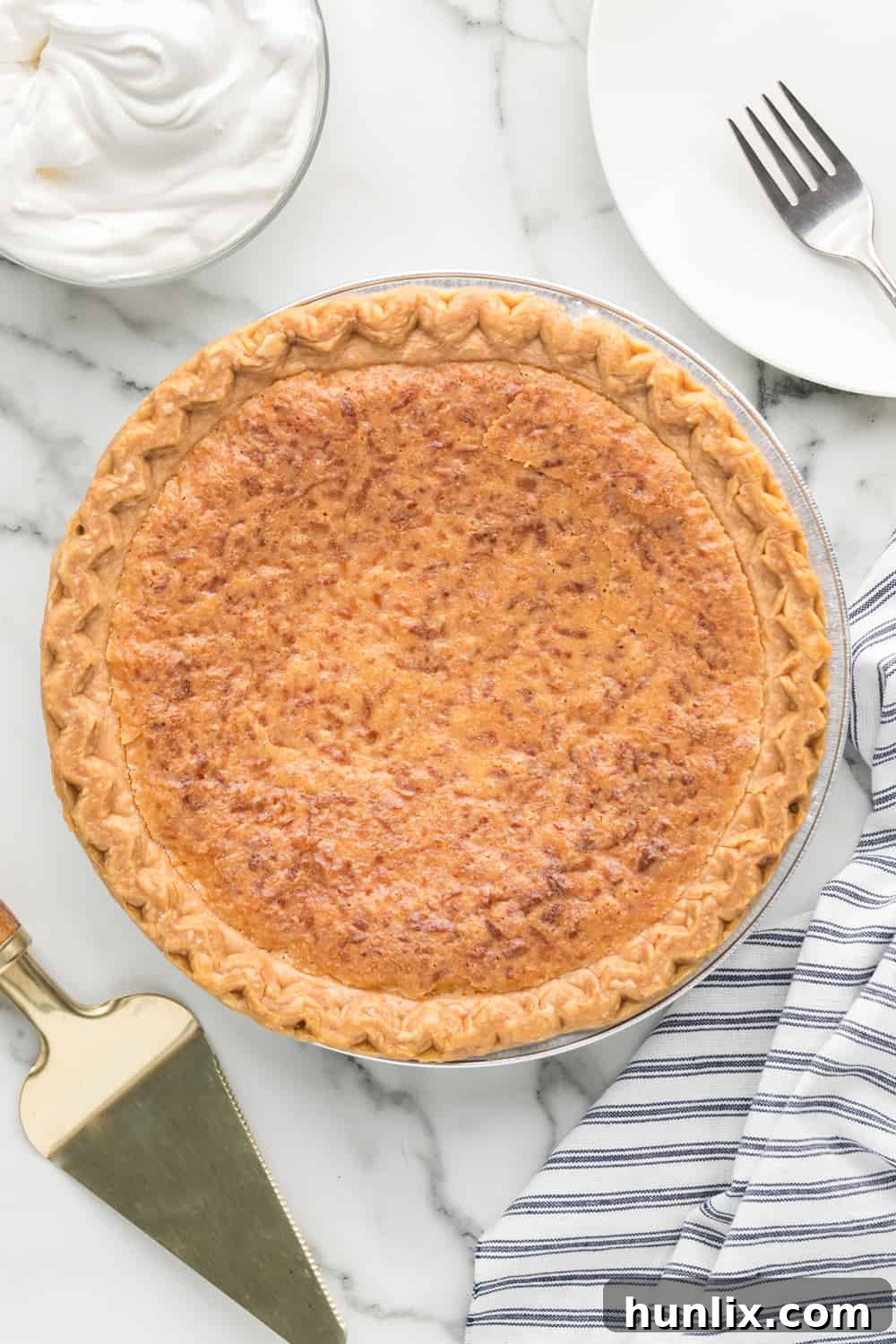 Luscious Coconut Cream Pie 2 Whole baked coconut pie on a white counter, ready to be sliced and served.