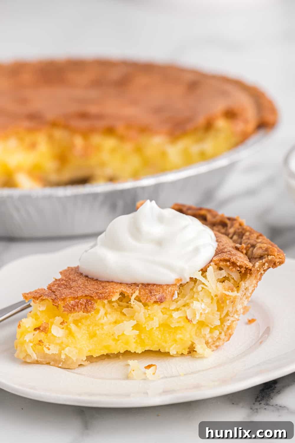 Luscious Coconut Cream Pie 8 A slice of coconut pie topped with a generous swirl of whipped cream on a white plate.