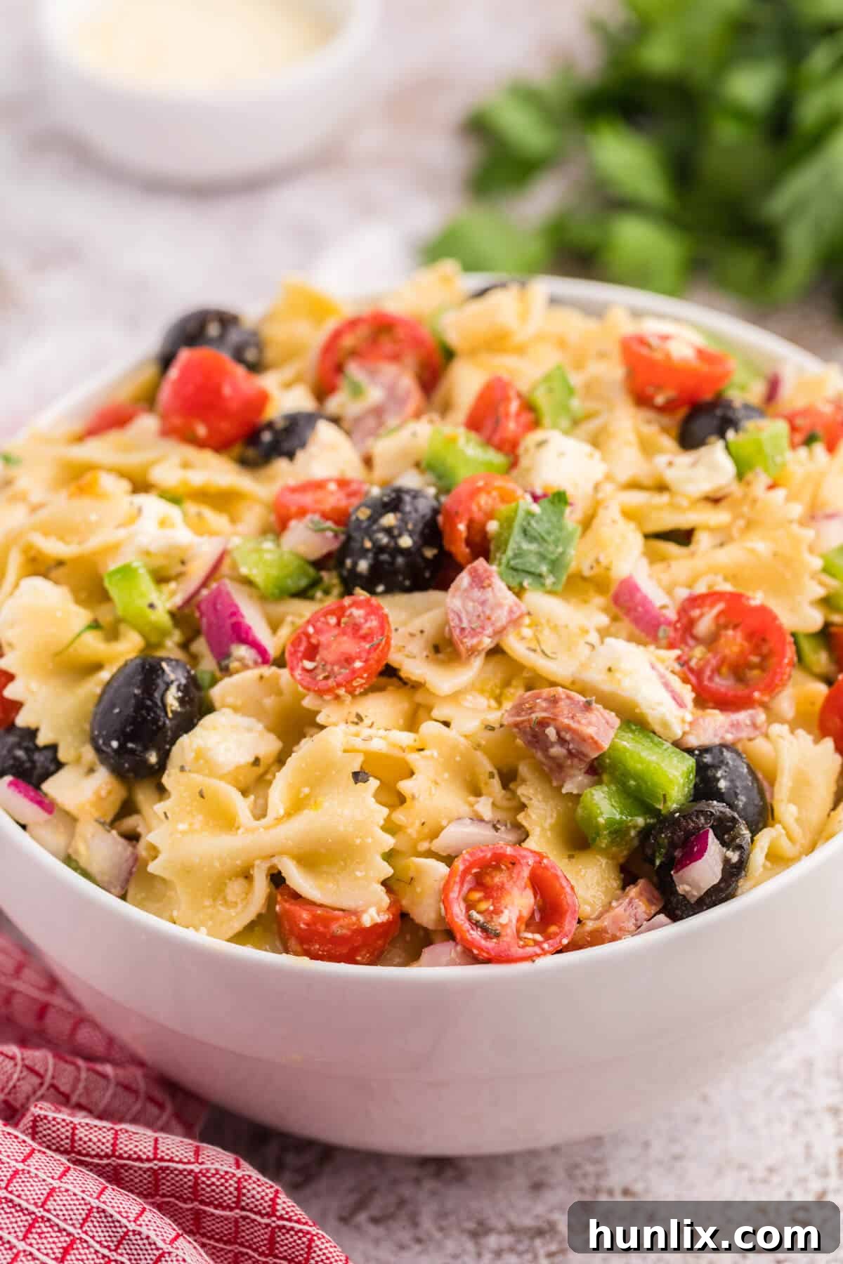 A large white bowl filled with Italian pasta salad, ready to be served on a rustic wooden table.