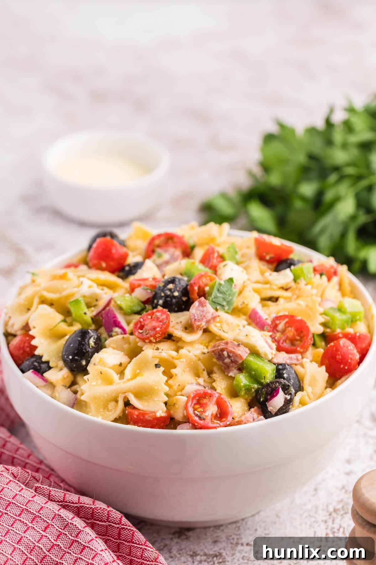 A white bowl of Italian pasta salad placed on a table with a red napkin beside it, ready to be enjoyed.