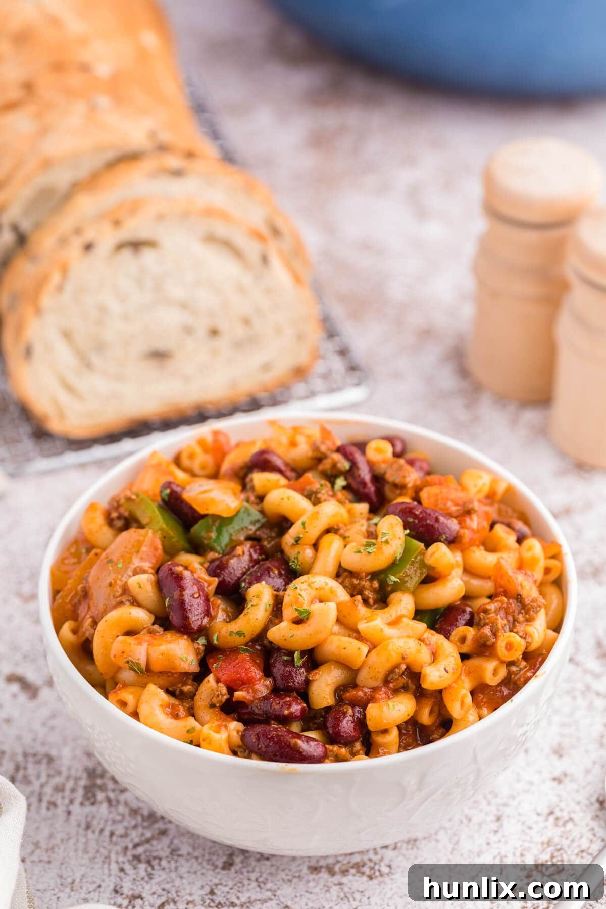 A white bowl filled with Chili Macaroni, garnished with fresh herbs, ready to be enjoyed.