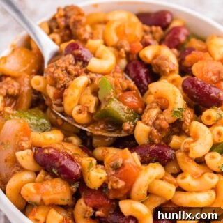 A white bowl with Chili Macaroni and a spoon.