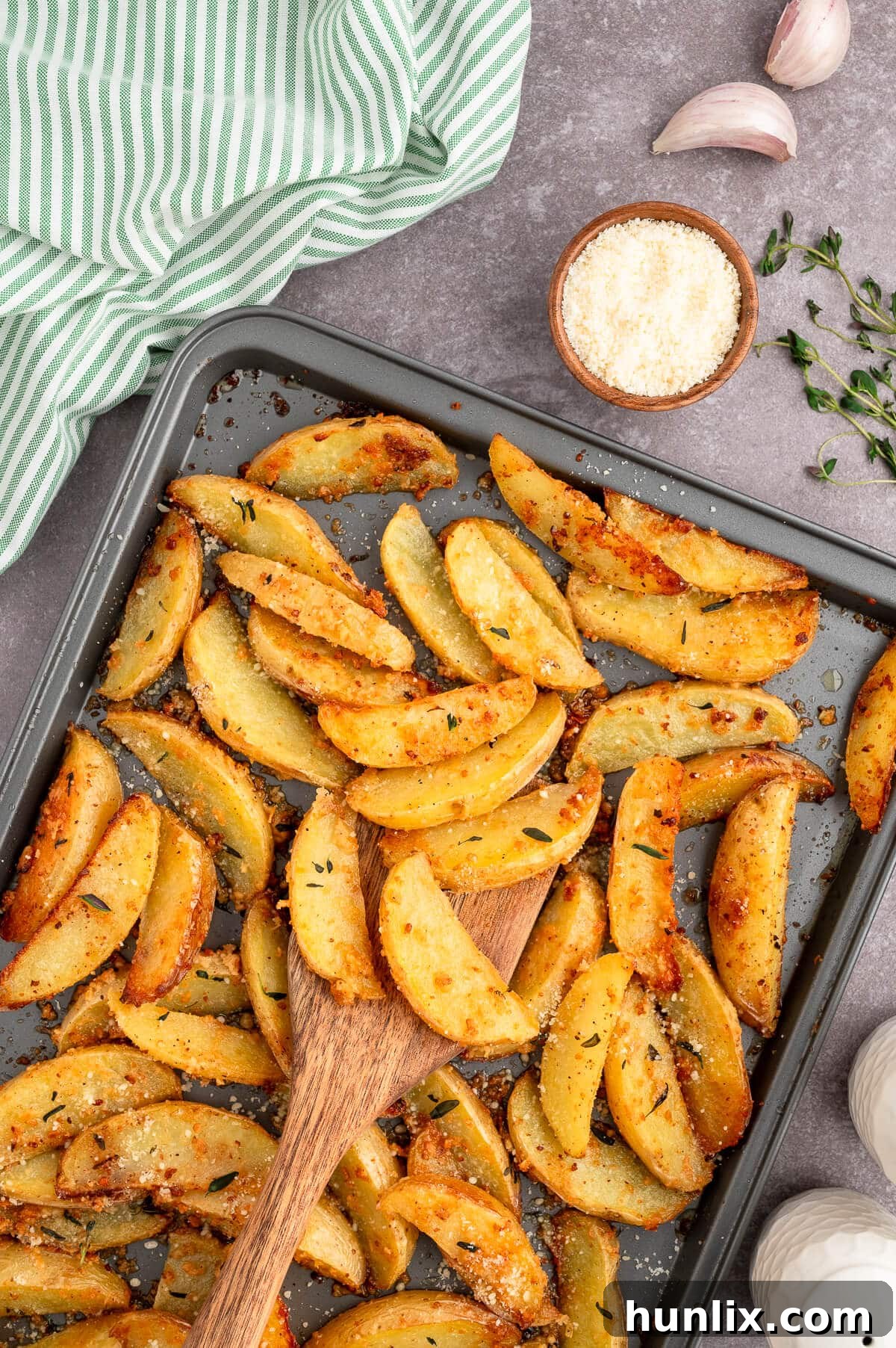 Parmesan thyme roasted potatoes glistening with herbs and cheese on a baking sheet, with a wooden spatula poised to serve.