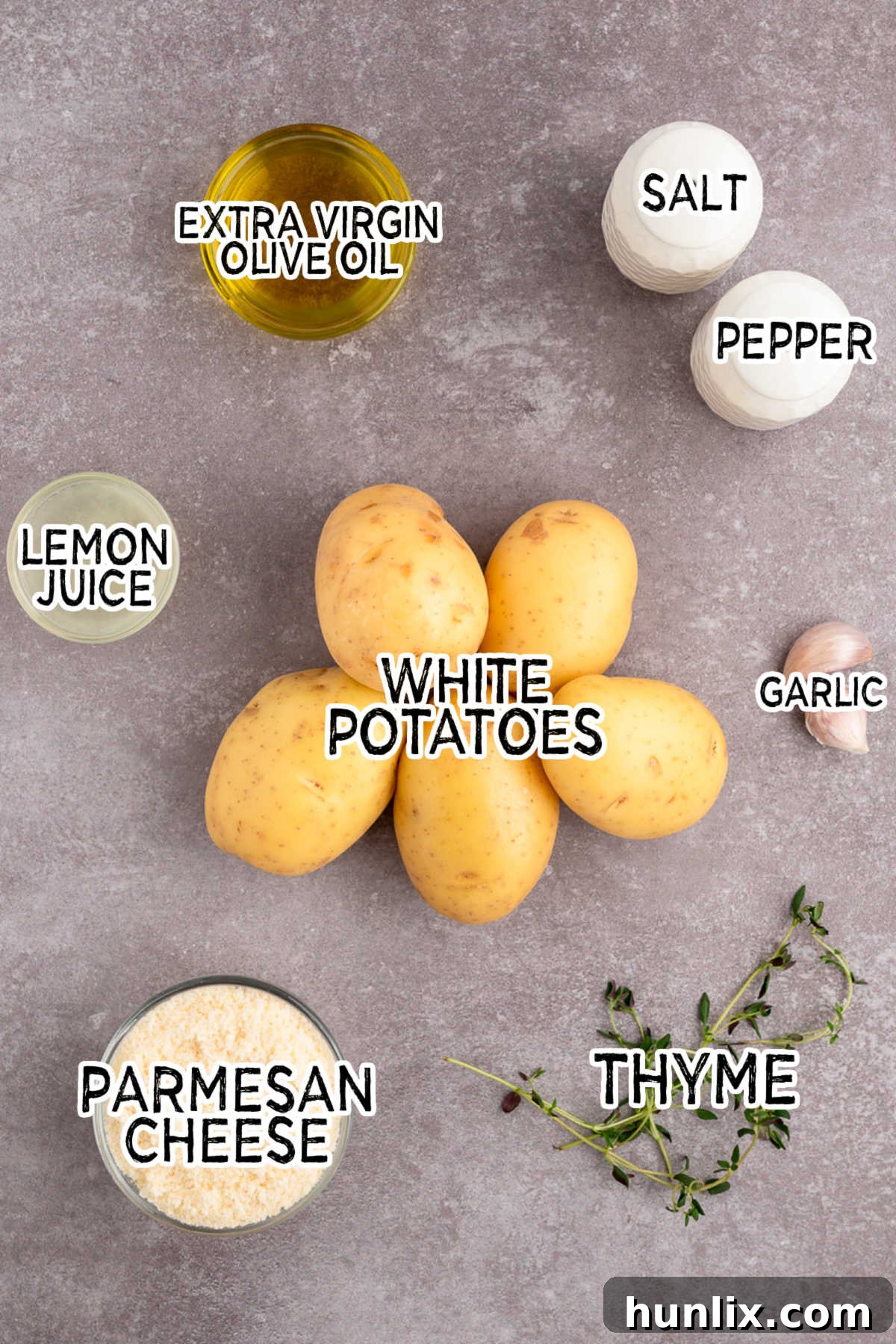 A vibrant flat lay of ingredients: whole white potatoes, a block of Parmesan cheese, a bunch of fresh thyme, bright lemons, garlic cloves, and a bottle of olive oil, all ready for preparation.