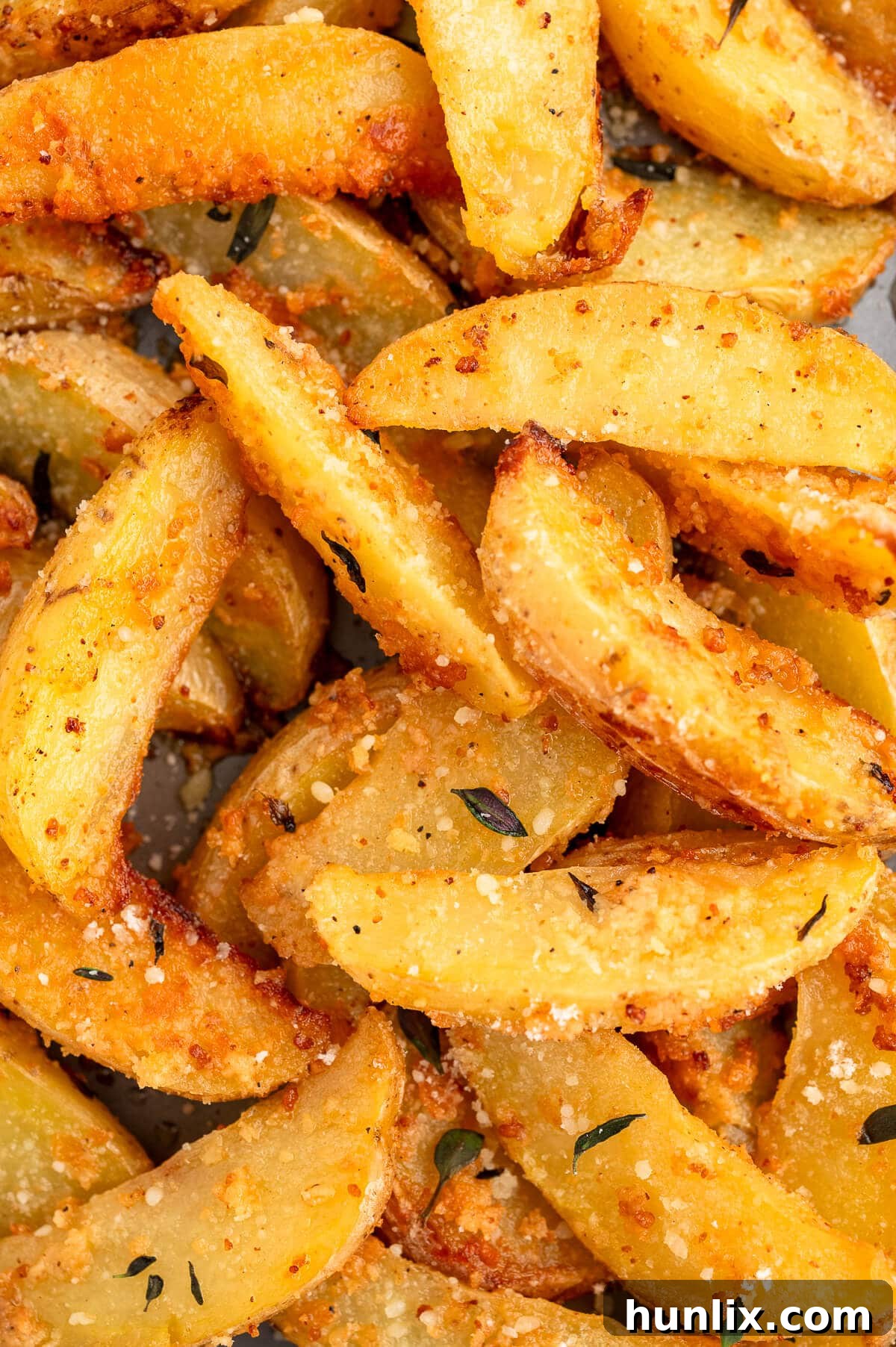 A close-up shot revealing the crispy, golden-brown skin and delicate herb flakes on a single Parmesan thyme roasted potato wedge.