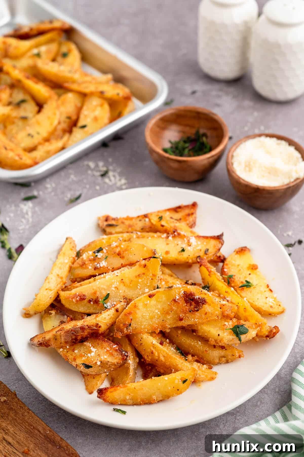 A beautifully plated serving of Parmesan thyme roasted potatoes, garnished with a sprig of fresh thyme, on a clean white plate.