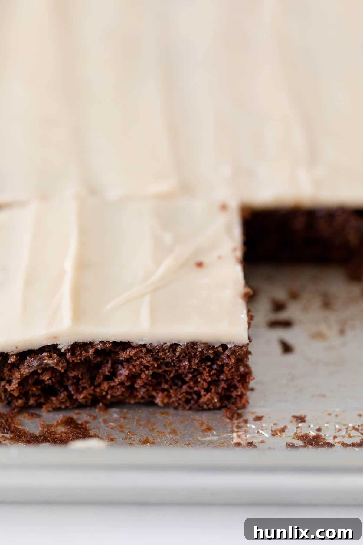 A large root beer float sheet cake in a rectangular pan with several squares already cut out, showing its moist chocolate layers and creamy frosting.
