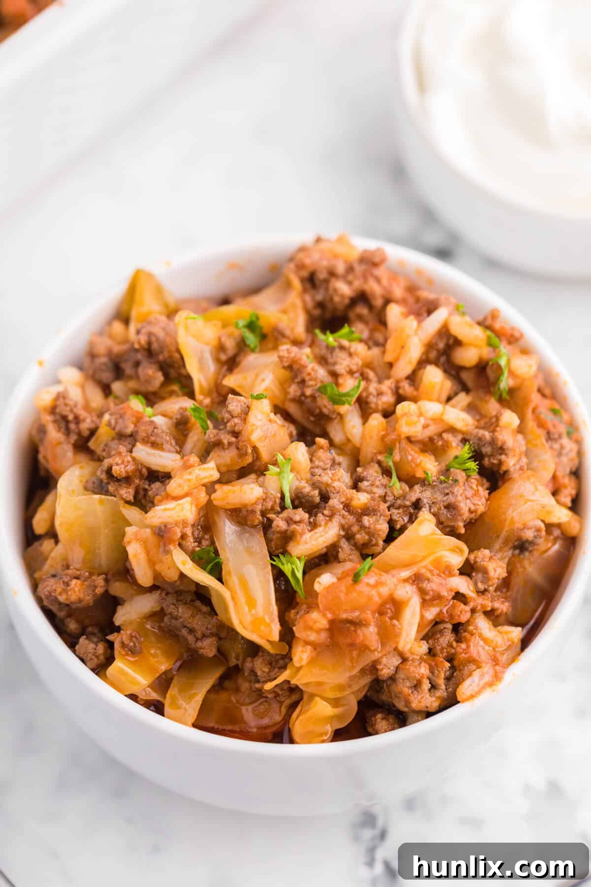 A white bowl filled with a generous serving of Cabbage Roll Casserole, showcasing its rich tomato sauce, ground beef, and tender cabbage layers.