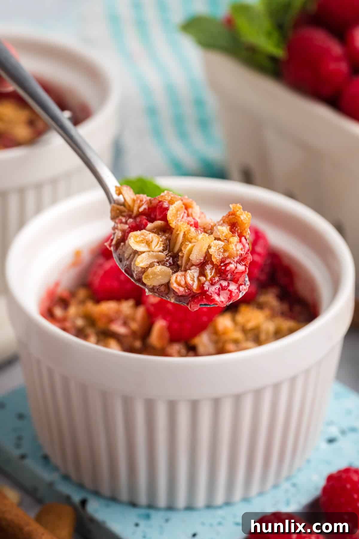 A spoon digging into a warm individual raspberry crisp in a ramekin.