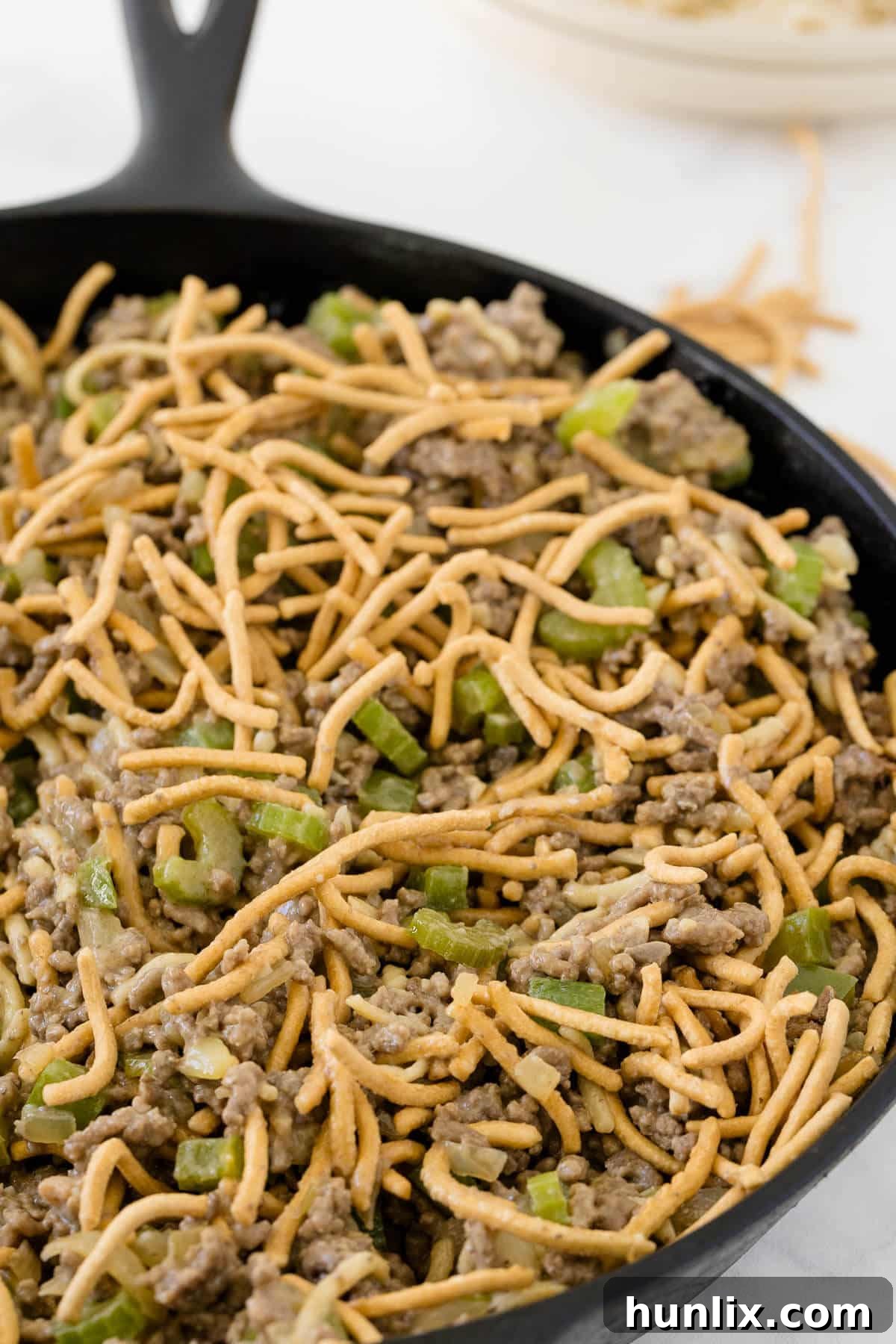 One-Pan Chow Mein 5 A close-up shot of the finished Chow Mein Skillet in a cast iron pan, showing the rich beef and vegetable mixture topped with crispy chow mein noodles.