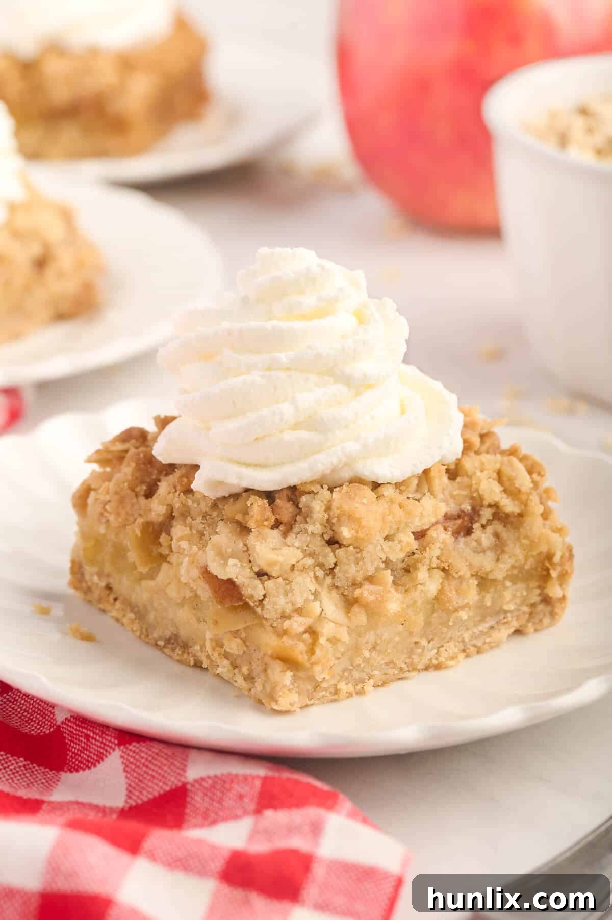 A perfectly portioned apple crisp bar, adorned with a swirl of fresh whipped cream, resting on a white plate, ready to be enjoyed.