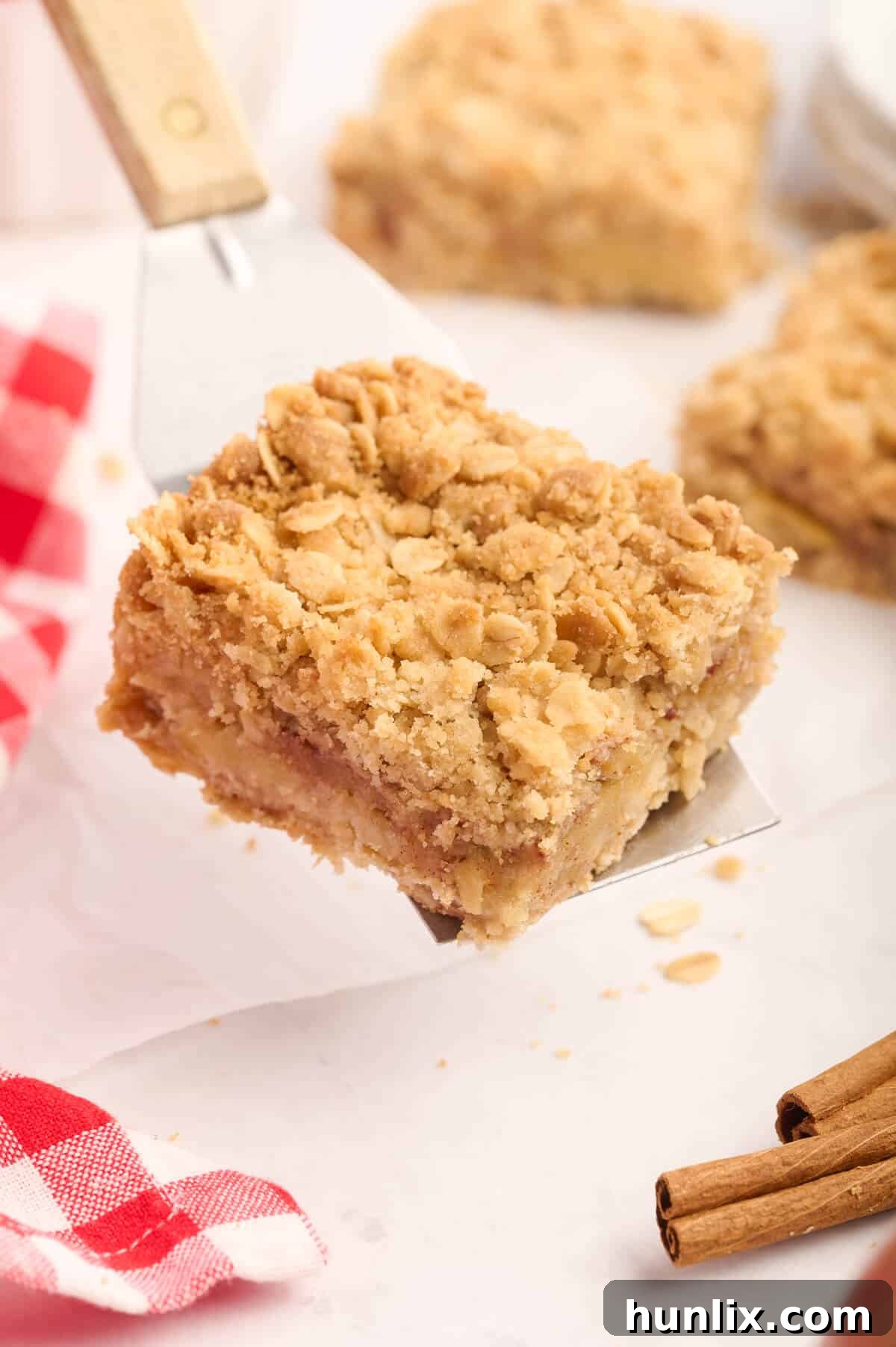 A single, golden-brown apple crisp bar being lifted from a pan with a serving spatula, ready to be plated.