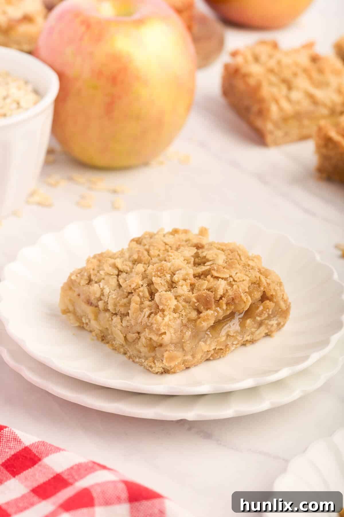 A perfect slice of apple crisp bar, with visible layers of oat crust, apple filling, and streusel topping, presented on a simple white plate.