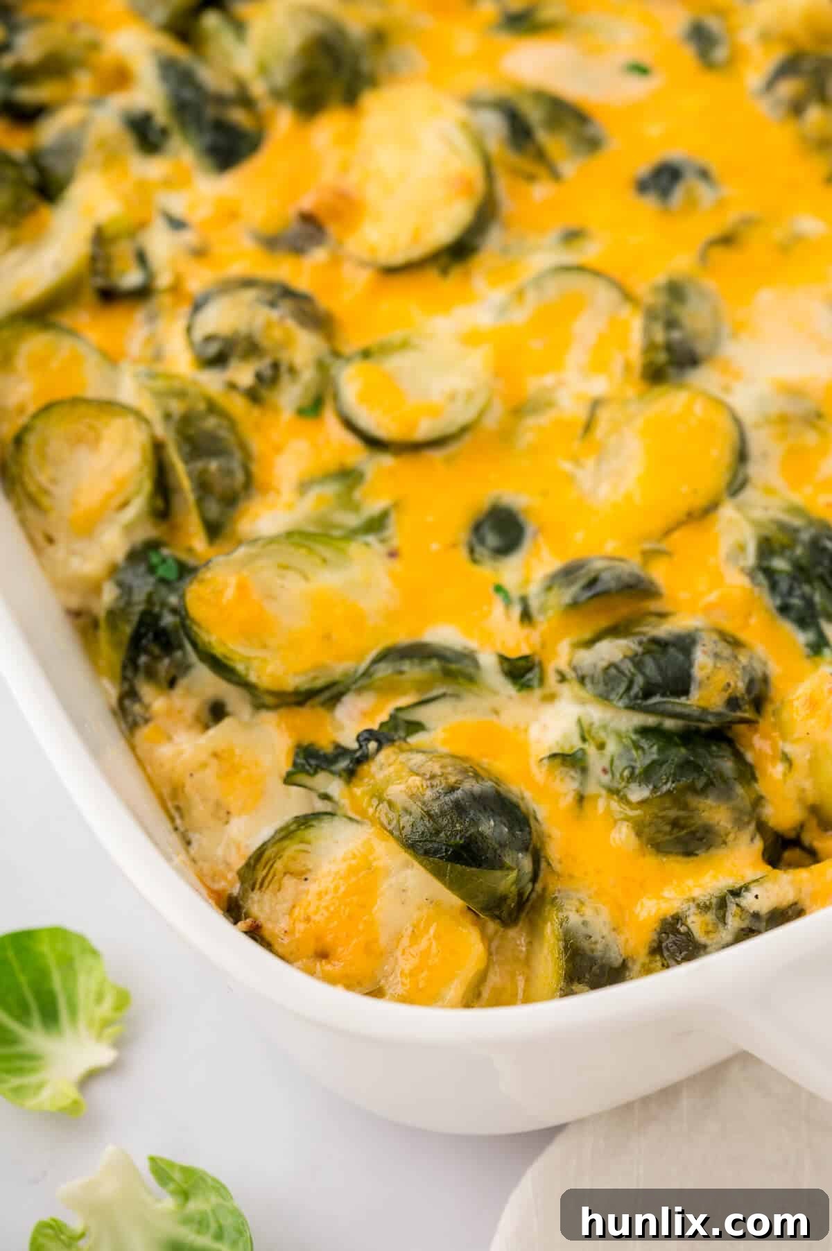 A golden-brown casserole dish filled with bubbling cheesy Brussels sprouts, garnished with fresh herbs.