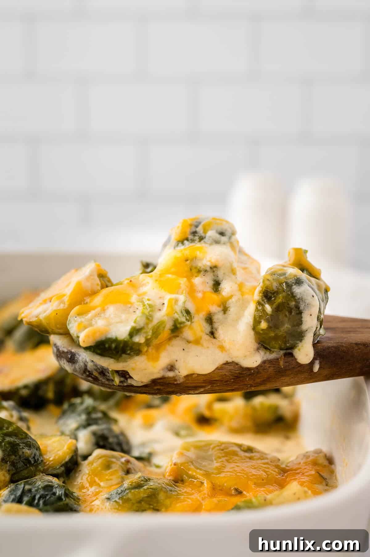 A wooden spoon scooping a portion of cheesy Brussels sprouts from a casserole dish, highlighting the creamy texture and melted cheese.