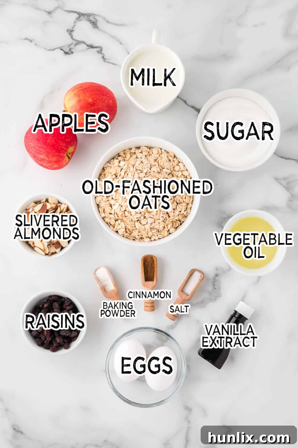 A beautiful flat lay of all the essential ingredients for baked oatmeal laid out on a marble counter, including oats, apples, raisins, almonds, milk, eggs, sugar, and spices, ready for assembly.