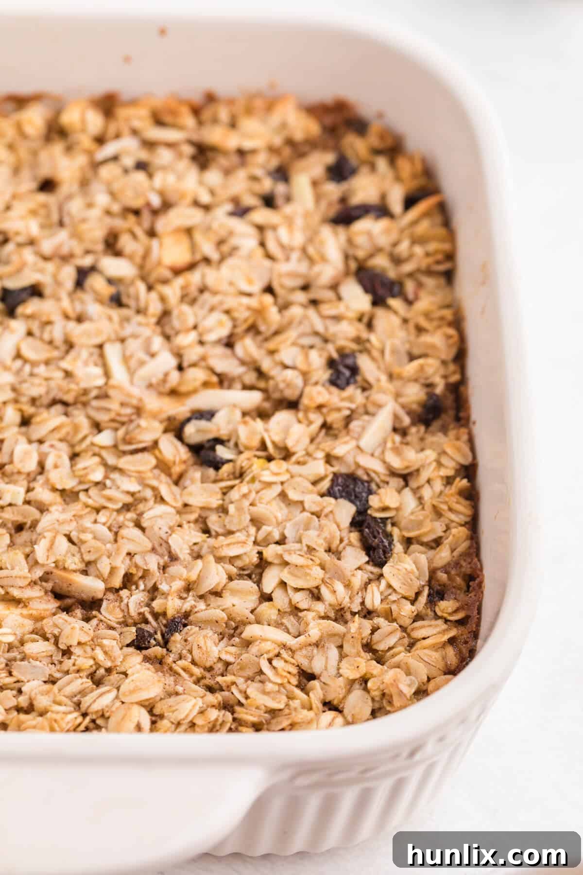 A golden-brown baked oatmeal casserole sits in a ceramic pan, garnished with a sprinkle of cinnamon and fresh fruit, ready to be served.