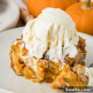 A piece of pumpkin bread pudding topped with vanilla ice cream on a plate with a fork.