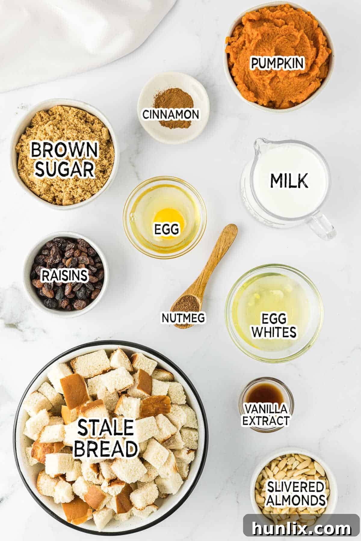 A vibrant selection of fresh ingredients neatly arranged for baking pumpkin bread pudding, including canned pumpkin puree, various spices, milk, and cubed stale bread.