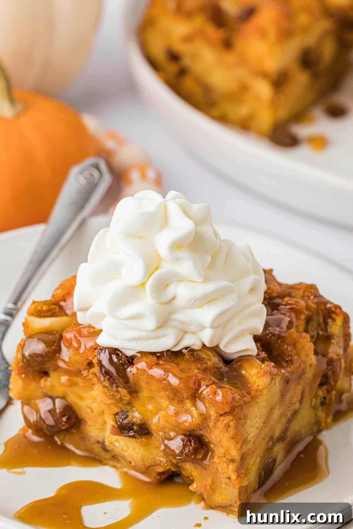 A serving of Pumpkin Bread Pudding luxuriously topped with a generous dollop of fluffy whipped cream and a light sprinkle of cinnamon.