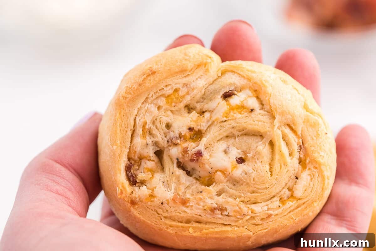 A close-up shot of a single Cheesy Bacon Pinwheel, showcasing its golden crust, melted cheese, and visible bacon bits, perfect for a party appetizer.