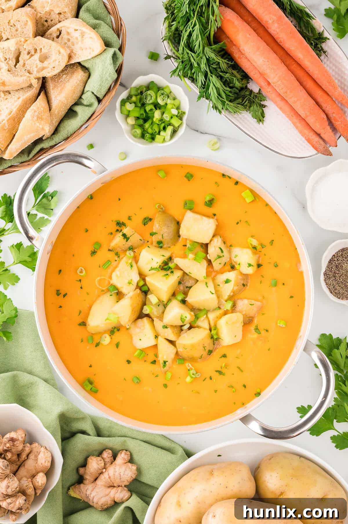 A pot of rich, golden carrot and potato soup, steaming gently and garnished with fresh herbs, ready to be served.