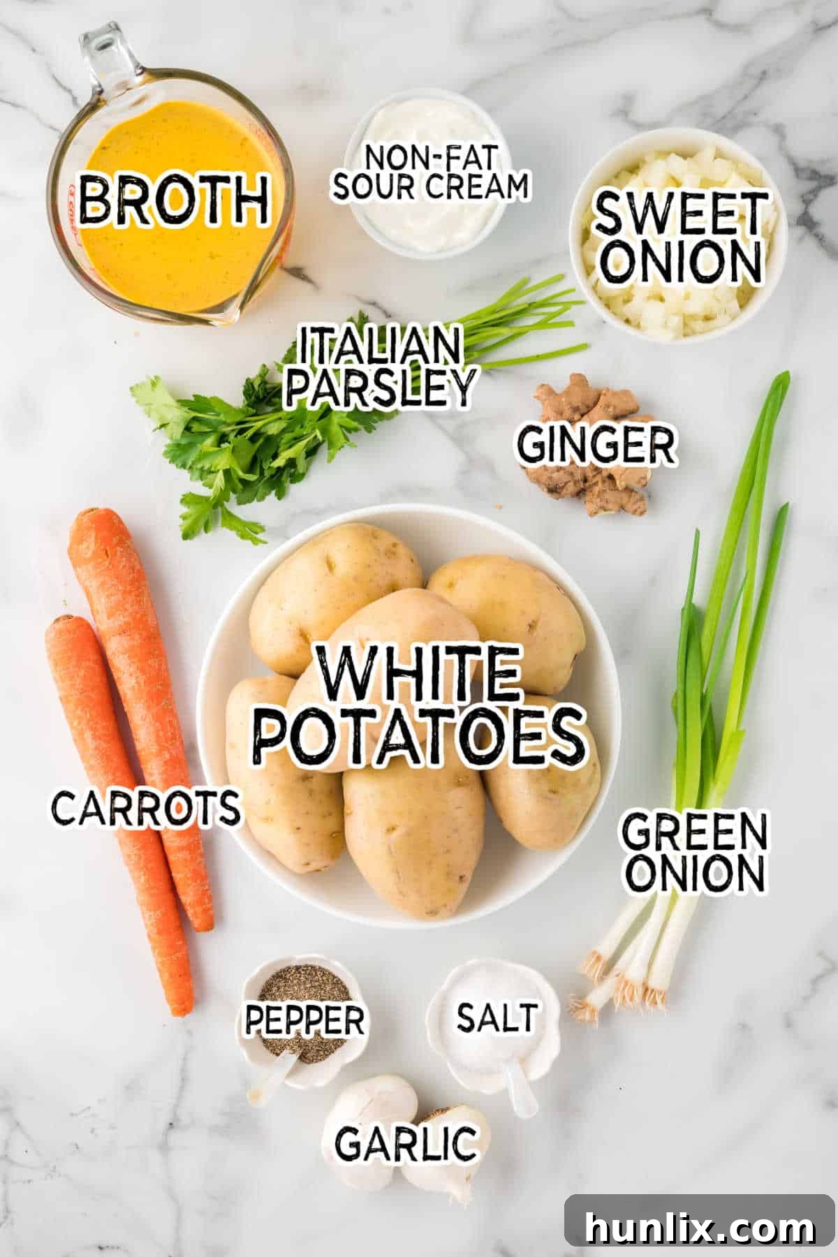 A vibrant collection of fresh ingredients laid out, including white potatoes, orange carrots, a sweet onion, garlic cloves, fresh ginger, green onions, and parsley, ready for making carrot and potato soup.