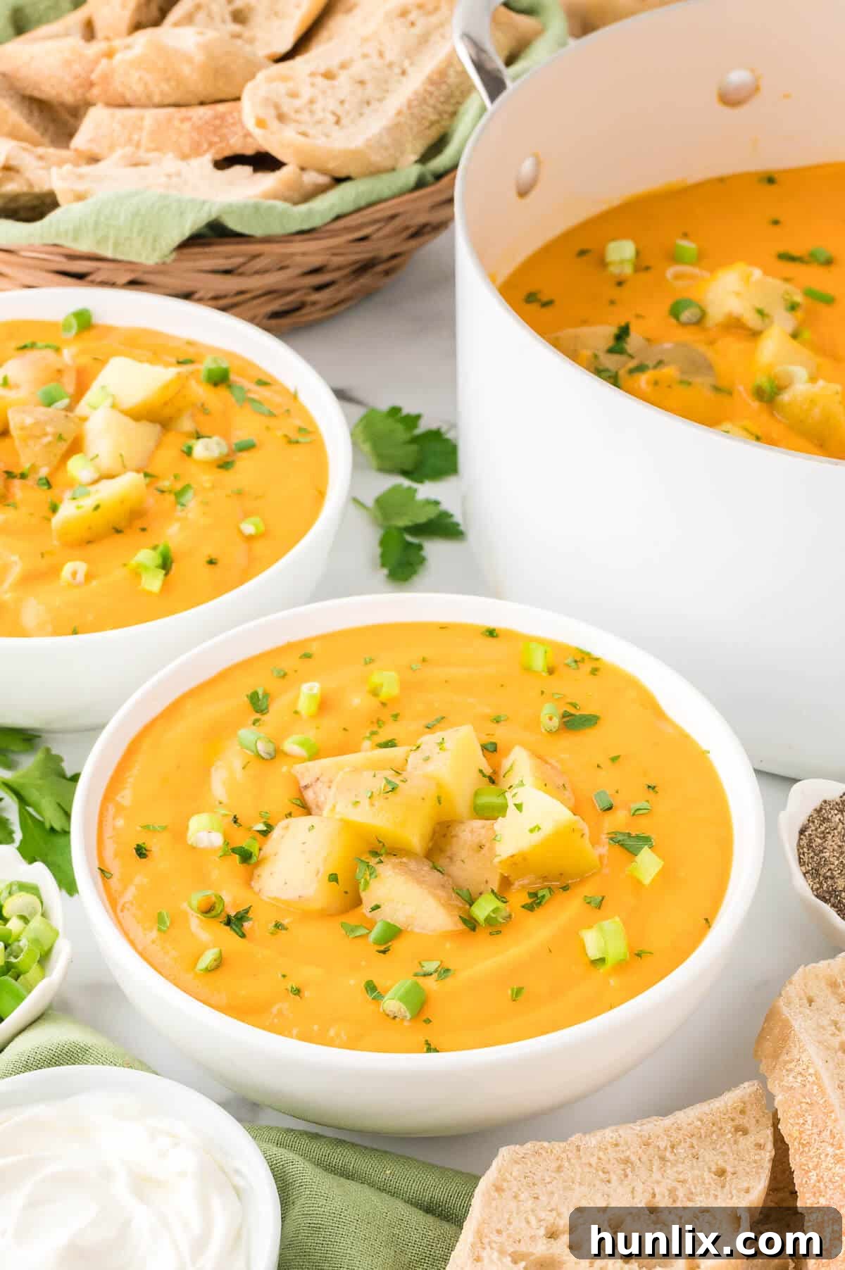 A pristine white bowl filled with creamy carrot and potato soup, garnished with delicate green herbs, on a light wooden surface.