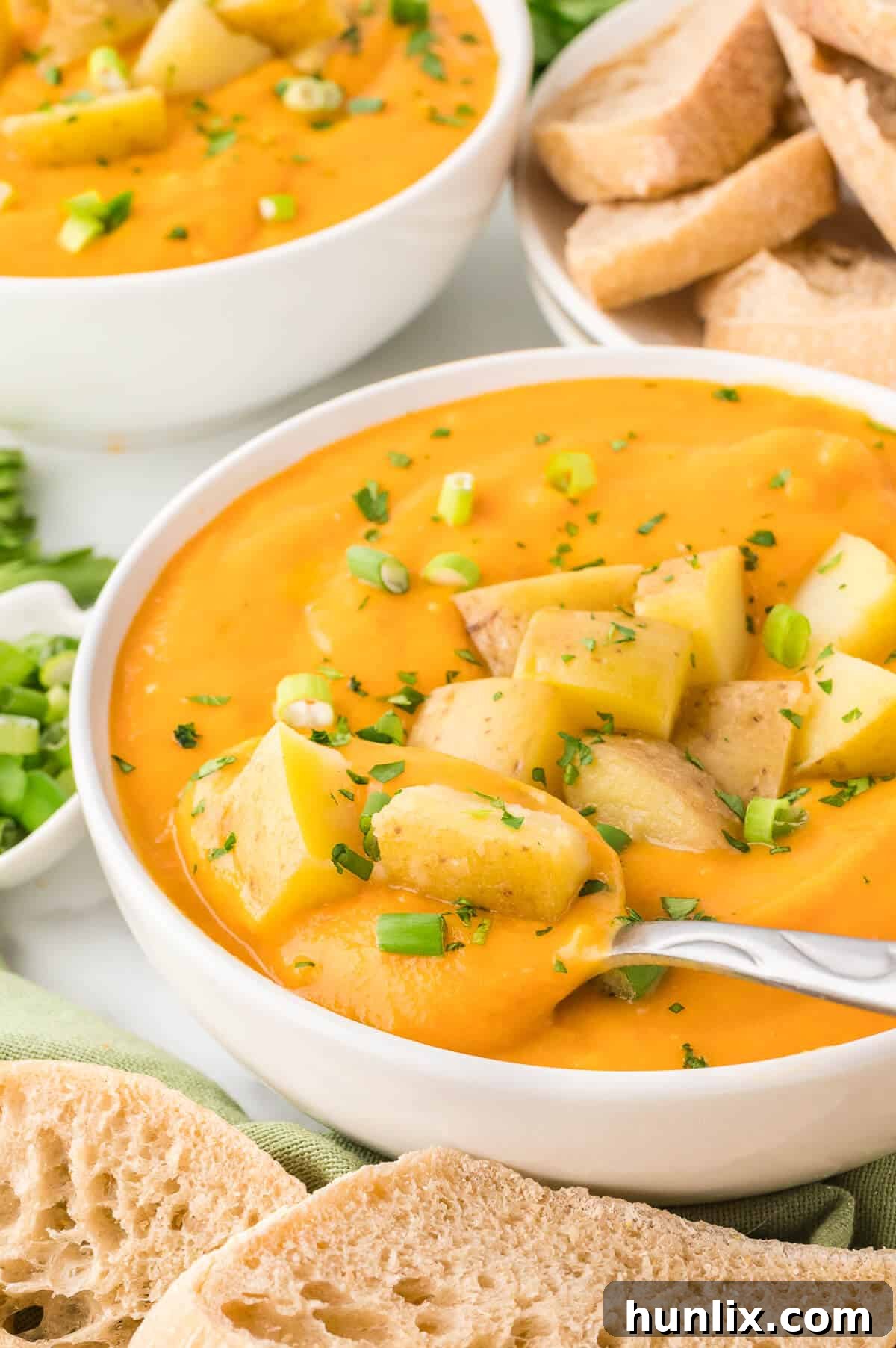 A white bowl of creamy carrot and potato soup with a spoon resting in it, surrounded by rustic elements.