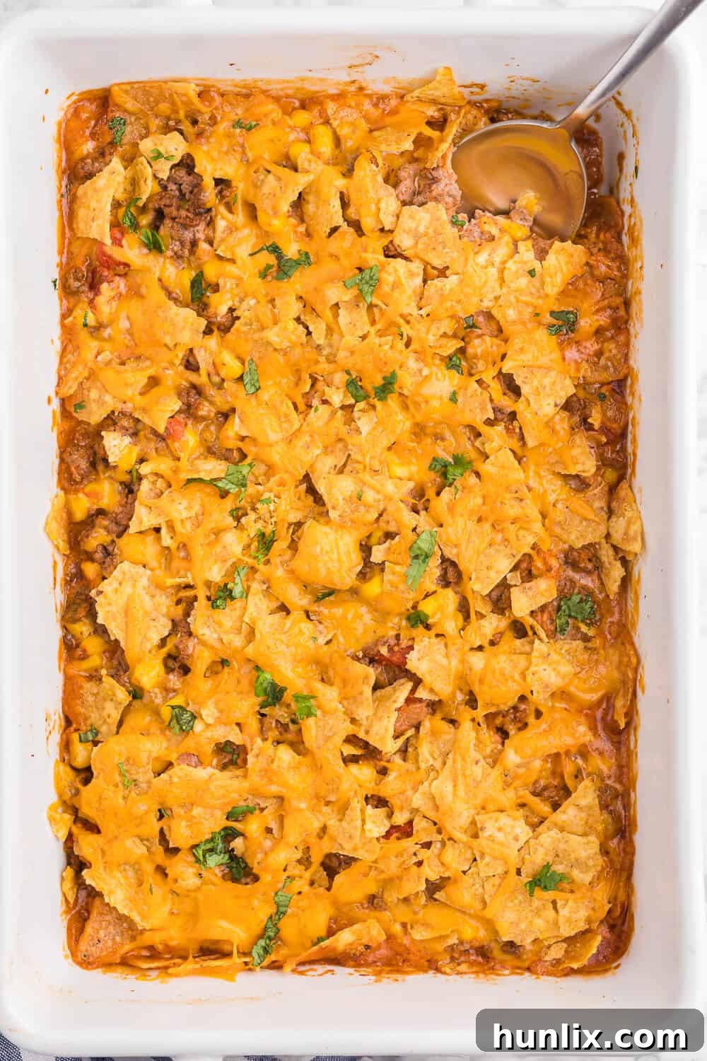 Fiesta Beef Nacho Bake 3 Beef nacho bake in a white casserole with a serving spoon, ready to be enjoyed.