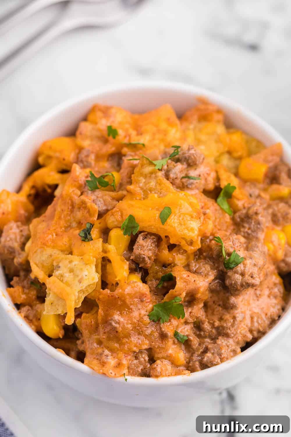Fiesta Beef Nacho Bake 6 Beef nacho bake in a white bowl, ready to be eaten, with a spoon.