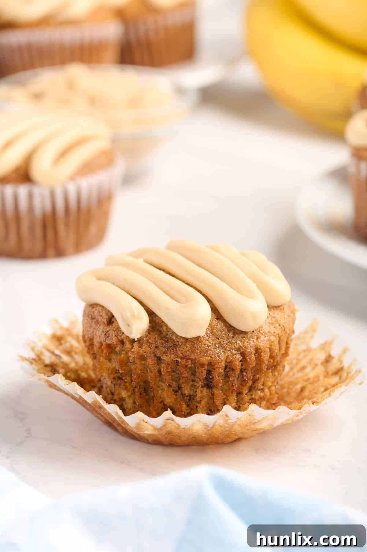 A close-up of a single caramel banana muffin still in its wrapper, inviting a bite.