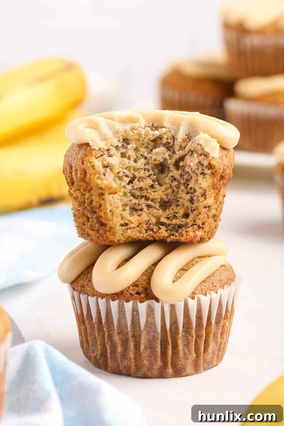 A stack of caramel banana muffins, with the top one having a bite taken out, revealing its moist interior.