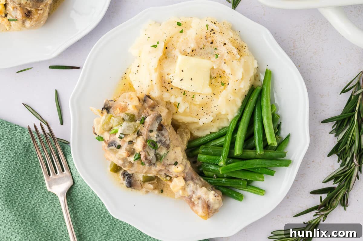 Tender Chicken in Rich Gravy 8 A close-up shot of a plate of smothered chicken, showing the creamy gravy, tender chicken, mashed potatoes, and green beans.