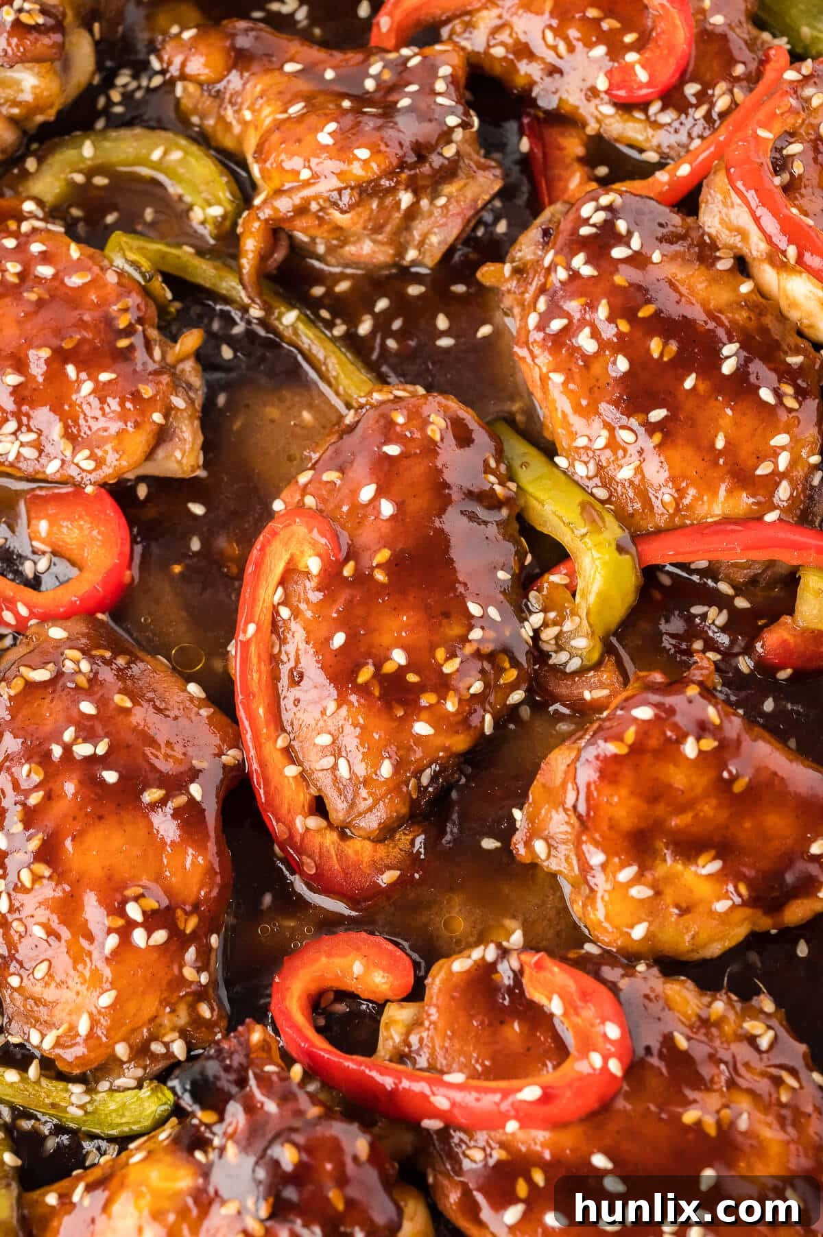 Crispy Asian chicken wings on a baking sheet, garnished with fresh sesame seeds and chopped bell peppers, highlighting their sticky hoisin glaze and golden-brown exterior.