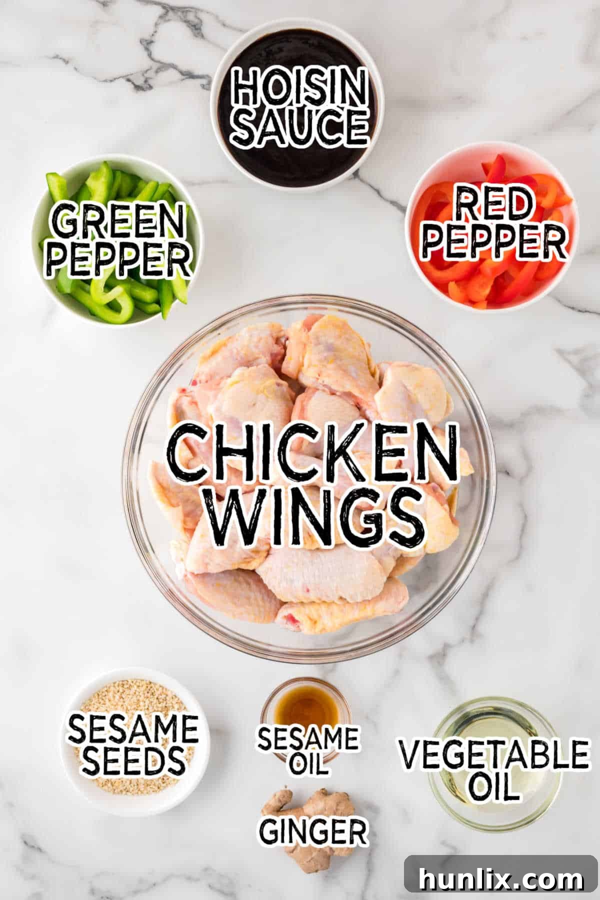 Various ingredients for Asian chicken wings including chicken wings, hoisin sauce, sesame seeds, ginger, vegetable oil, and bell peppers arranged on a white marble background.