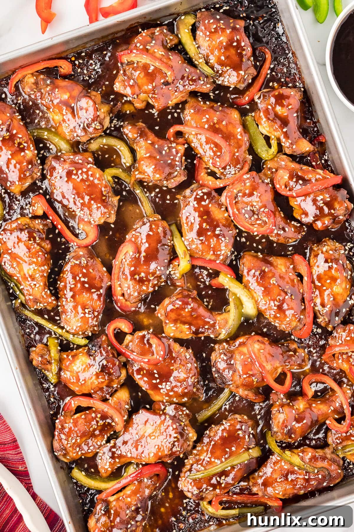 A close-up of baked Asian chicken wings on a baking sheet, glistening with hoisin glaze and sprinkled with sesame seeds, ready to be served.